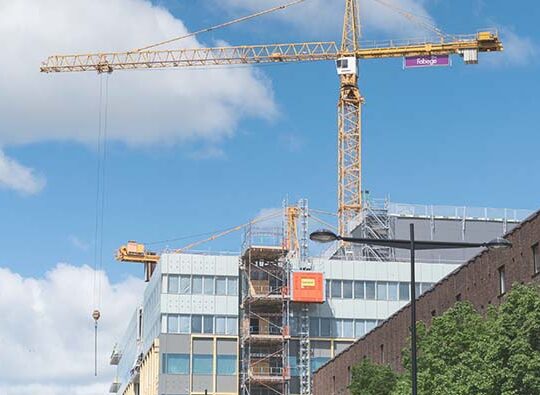 Mellan några fastigheter eller kontor skyns en stor byggkran,