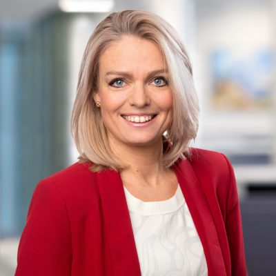 Porträtt framifrån på en kvinna i röd kavaj som ser in i kameran och ler.