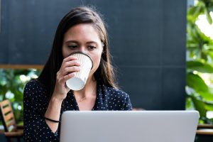 Kvinna dricker kaffe framför sin laptop