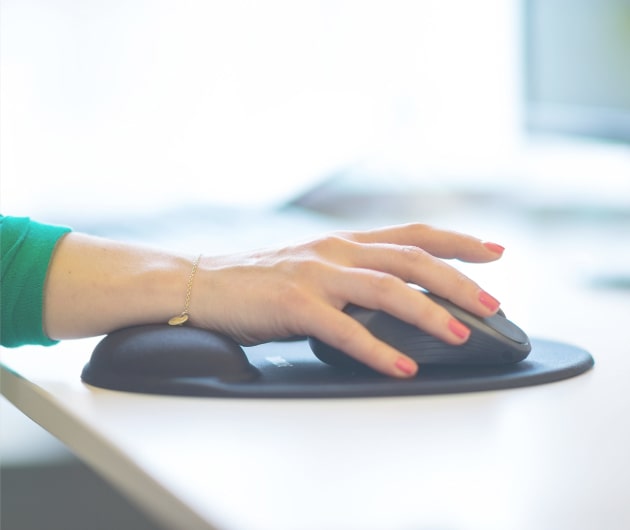 Detaljbild på en kvinnlig hand med målade naglar som håller i en datormus på ett vitt skrivbord.