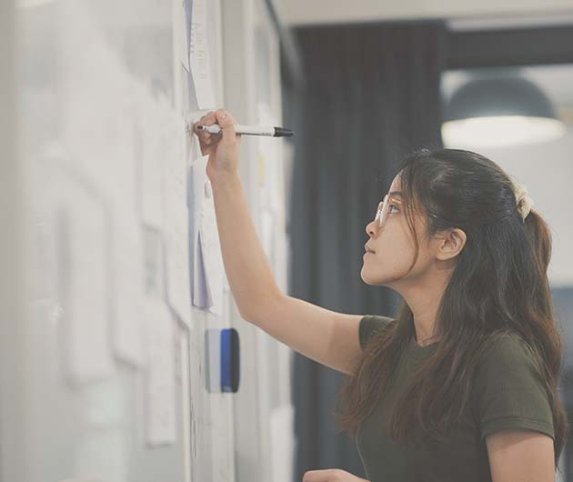 Ung kvinna, fotograferad från sidan, skriver på en whiteboardtavla.