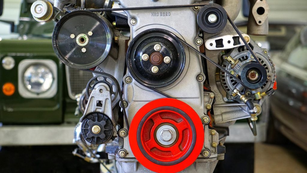 Detalj av en bilmotor med remmar och cylindrar.