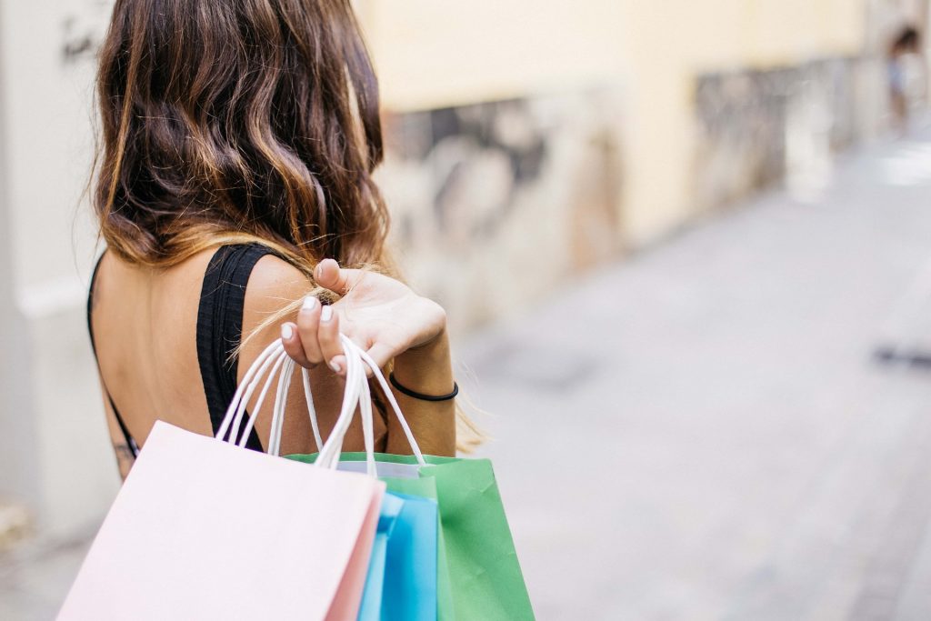 Ung kvinna med brunt långt hår sedd bakifrån håller upp en rad shoppingpåsar