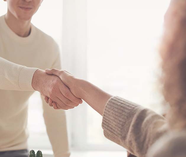 Närbild på två personer som skaka hand ovanför ett skrivbord.