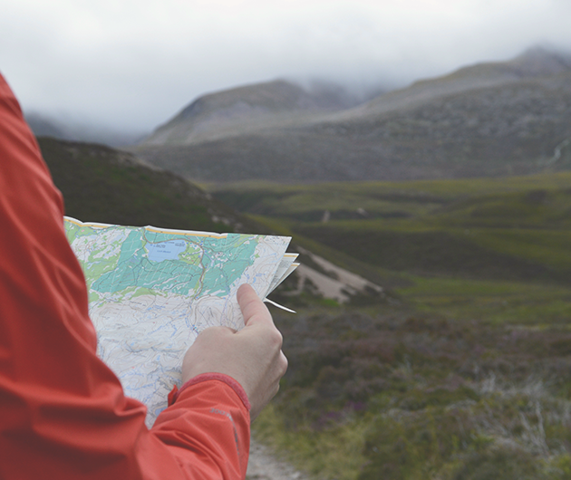 En person i röd jacka tittar på en orienteringskarta ute i naturen.