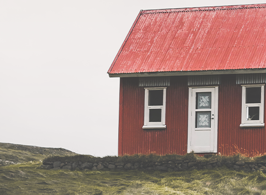 Ett litet rött trähus på ett grönt fält.