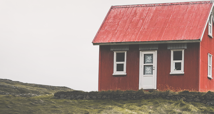 Ett litet rött trähus på ett grönt fält.