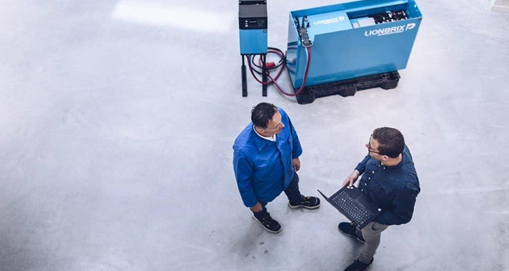 Två män pratar med varandra vid en städmaskin/robot som står på ett industrigolv.