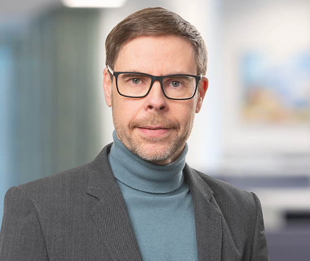 Porträtt på man i glasögon, polotröja och kavaj inne på ett kontor.