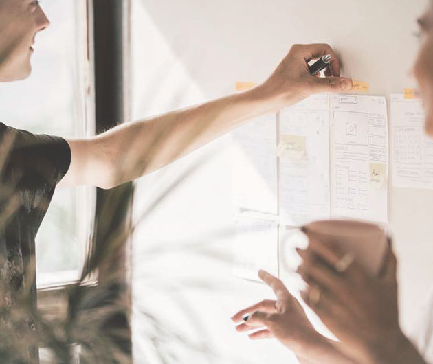 Två kvinnor jobbar vid en whiteboardtavla.