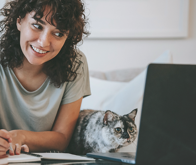 Ung kvinna i mörkt lockigt hår sneglar mot en datorskärm, ihop med sin katt.