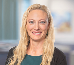 Porträtt på en kvinna med långt blont hår och grön tröja som ler in i kameran.