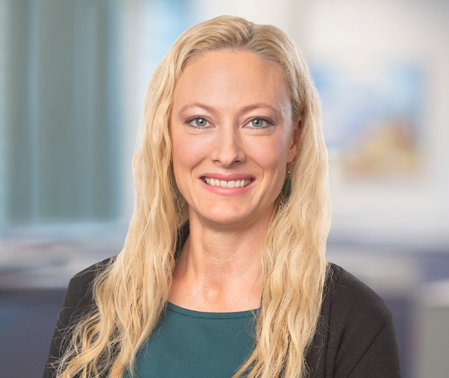 Porträtt på en kvinna med långt blont hår och grön tröja som ler in i kameran.