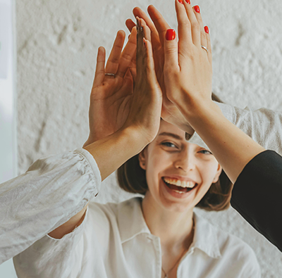Sex händer gör high-five, men man ser bara en av personerna, en kvinna, som ser glad ut.