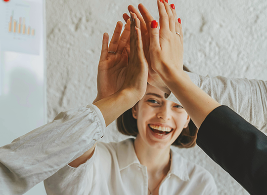 Sex händer gör high-five, men man ser bara en av personerna, en kvinna, som ser glad ut.