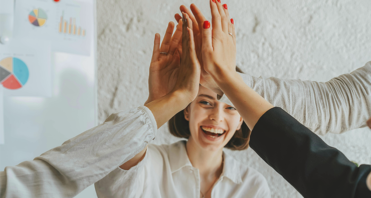 Sex händer gör high-five, men man ser bara en av personerna, en kvinna, som ser glad ut.