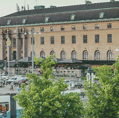 Vy över Göteborgs Centralstation med Clarion Post hotel i bakgrunden. Spårvagnar och gröna lummiga träd syns.